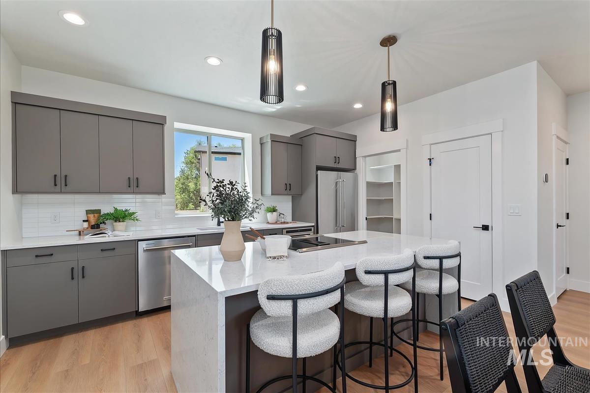 Kitchen with gray cabinetry, pendant lighting, stainless steel appliances, and light wood-style floors