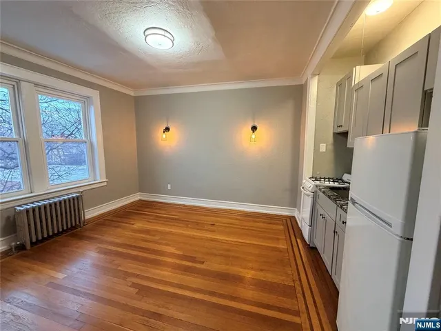 a view of kitchen and empty room with wooden floor