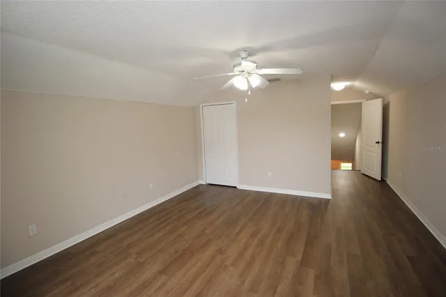 an empty room with wooden floor fan and windows