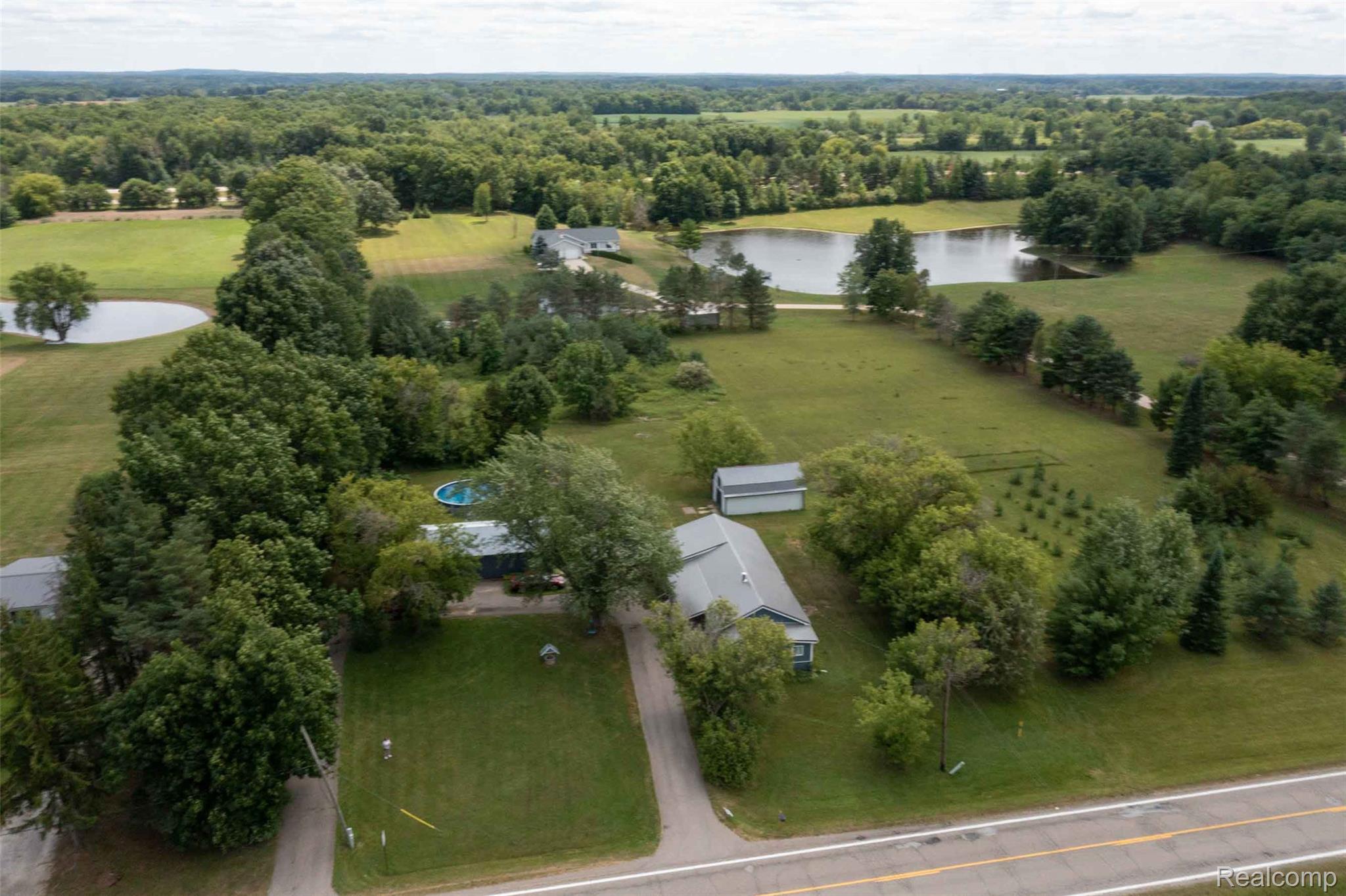 5761 Genesee Road Lapeer, MI 48446 - Photo 28 of 52 Expansive property featuring a residence with a gray roof, a separate shed, an above-ground pool, and a large pond