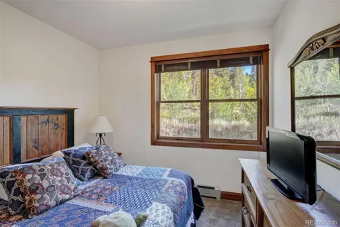 a bedroom with a bed window and a flat tv screen on dresser