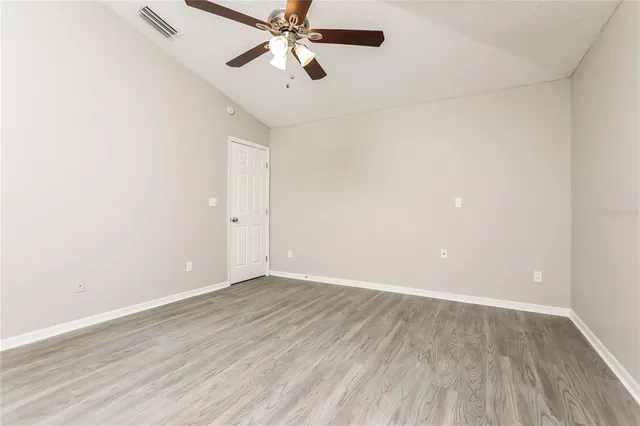 an empty room with wooden floor fan and windows