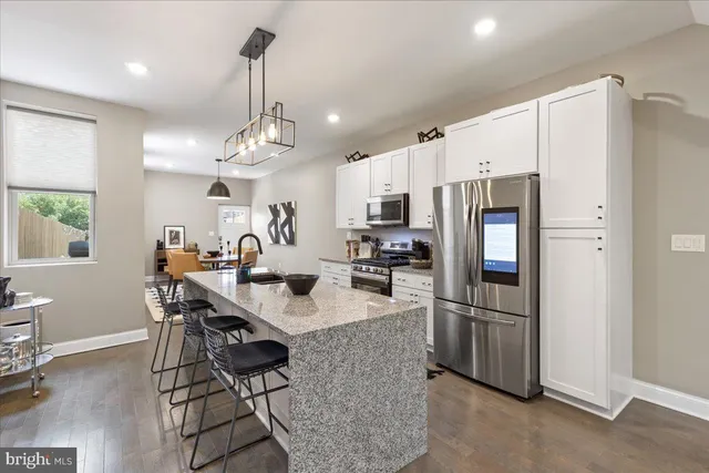 a kitchen with stainless steel appliances granite countertop a refrigerator a sink dishwasher a stove a dining table and chairs with wooden floor