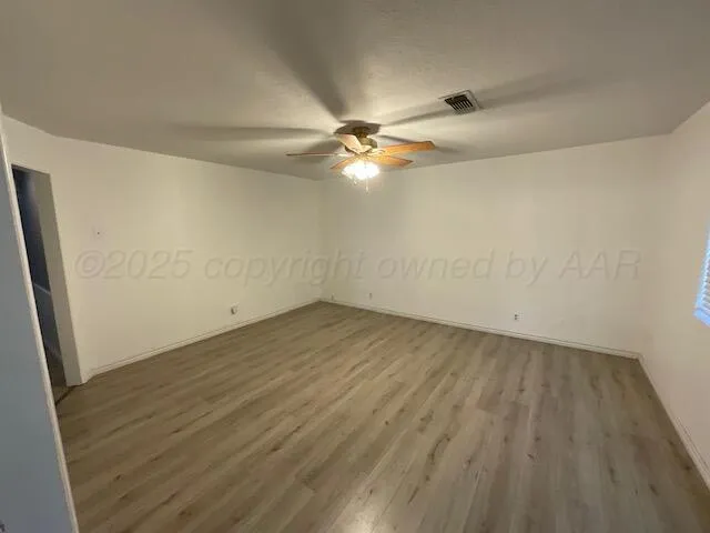 an empty room with wooden floor and fan