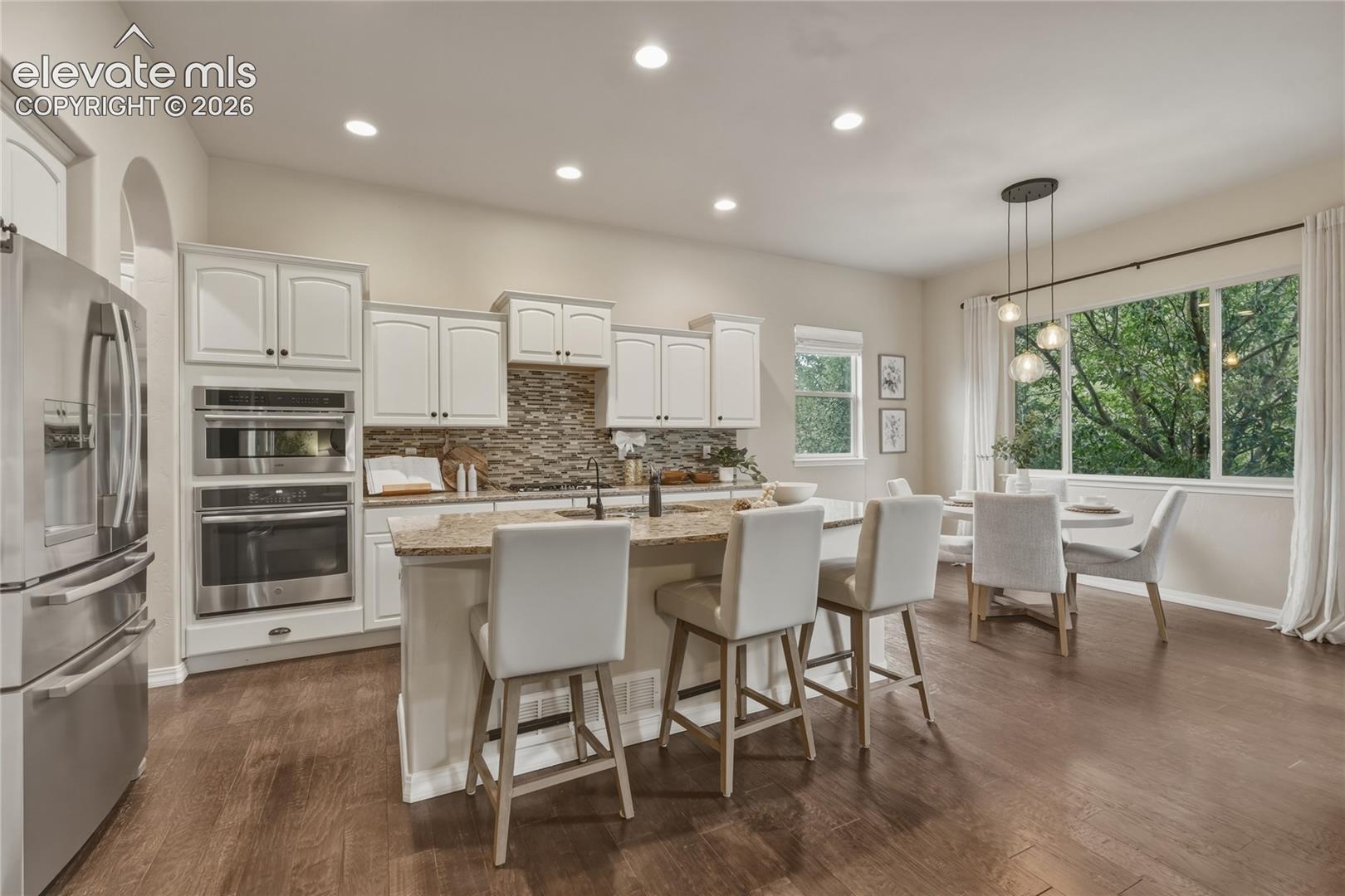 1118 Spectrum Loop Colorado Springs, CO 80921 - Photo 10 of 50 Open-concept kitchen with wood-finish flooring, white cabinetry, stainless steel appliances, a center island with seating, and a dining area with expansive windows