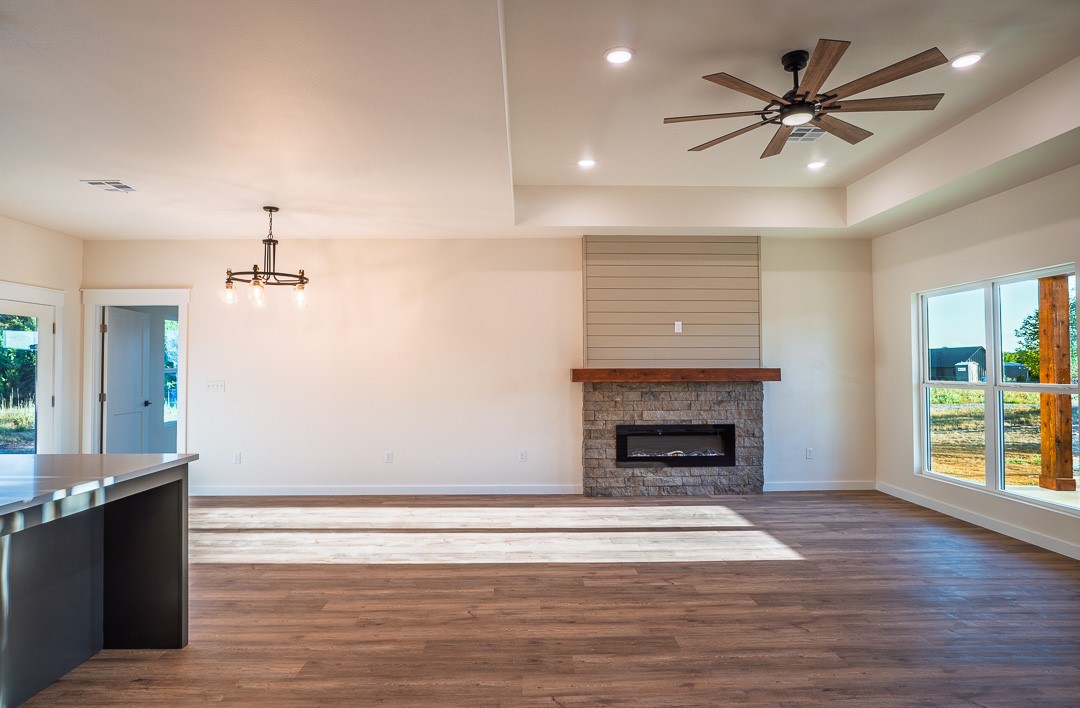205 Blessings Way Colbert, OK 74733 - Photo 9 of 24 Spacious living area featuring wood-finish flooring, a stone-faced fireplace with wood mantel, multiple recessed lights, a modern ceiling fan, and large windows