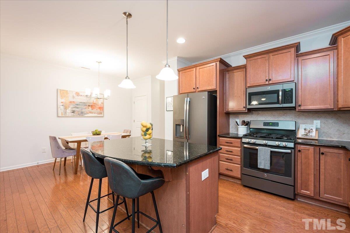 2405 Swans Rest Way Raleigh, NC 27606 - Photo 8 of 29 a kitchen with stainless steel appliances granite countertop a stove a refrigerator a kitchen island a dining table and chairs with wooden floor