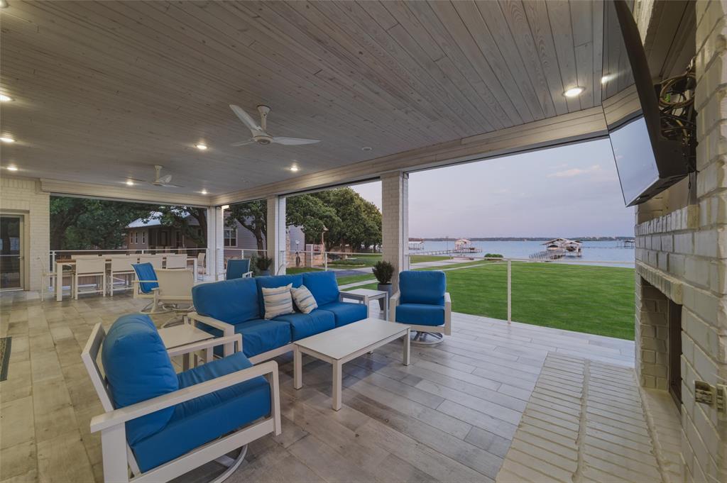 6625 Sandy Beach Road Azle, TX 76020 - Photo 26 of 40 Covered patio overlooks the waterfront setting with expansive open-air views across the lawn, dock access, and surrounding shoreline. Exterior fireplace with mounted television niche creates an additional outdoor gathering area beneath the covered patio structure.