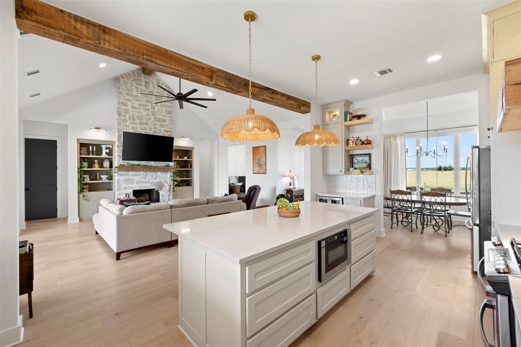 861 Brindley Road Maypearl, TX 76064 - Photo 10 of 36 Open-concept living space with vaulted ceilings, exposed wood beams, a stone fireplace, wood-finish flooring, and a kitchen island with built-in microwave