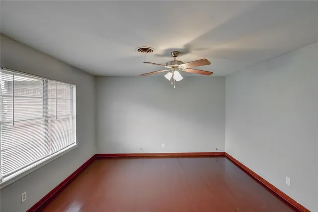 an empty room with wooden floor chandelier fan and windows