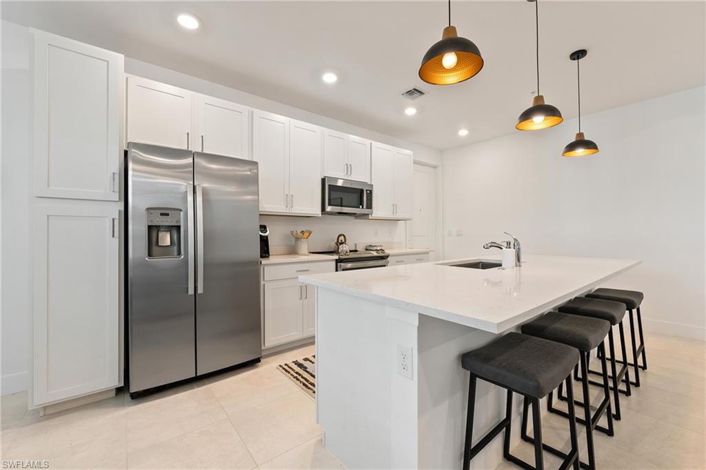26401 Coco Cay Circle, Unit 101 Bonita Springs, FL 34135 - Photo 4 of 27 a kitchen with stainless steel appliances granite countertop a sink a stove a refrigerator a microwave oven with a dining table and chairs