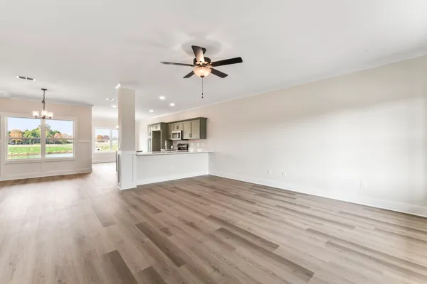 an empty room with wooden floor kitchen view and a window