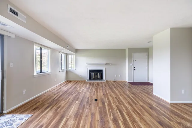 a view of an empty room with wooden floor fireplace and a window