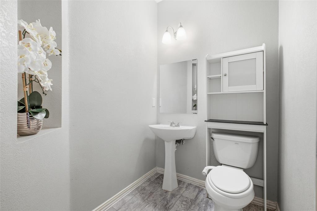 3903 Rive Lane Addison, TX 75001 - Photo 17 of 40 A clean, classic half bath on the main level features a pedestal sink, sconce lighting, framed mirror, and a decorative wall niche — everything guests need without any wasted space.