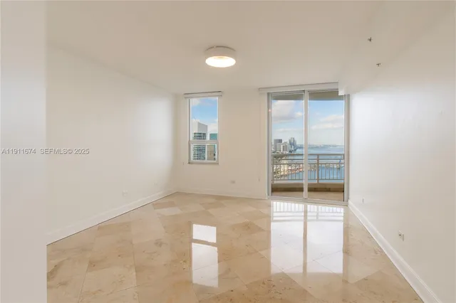 an empty room with windows and way to kitchen