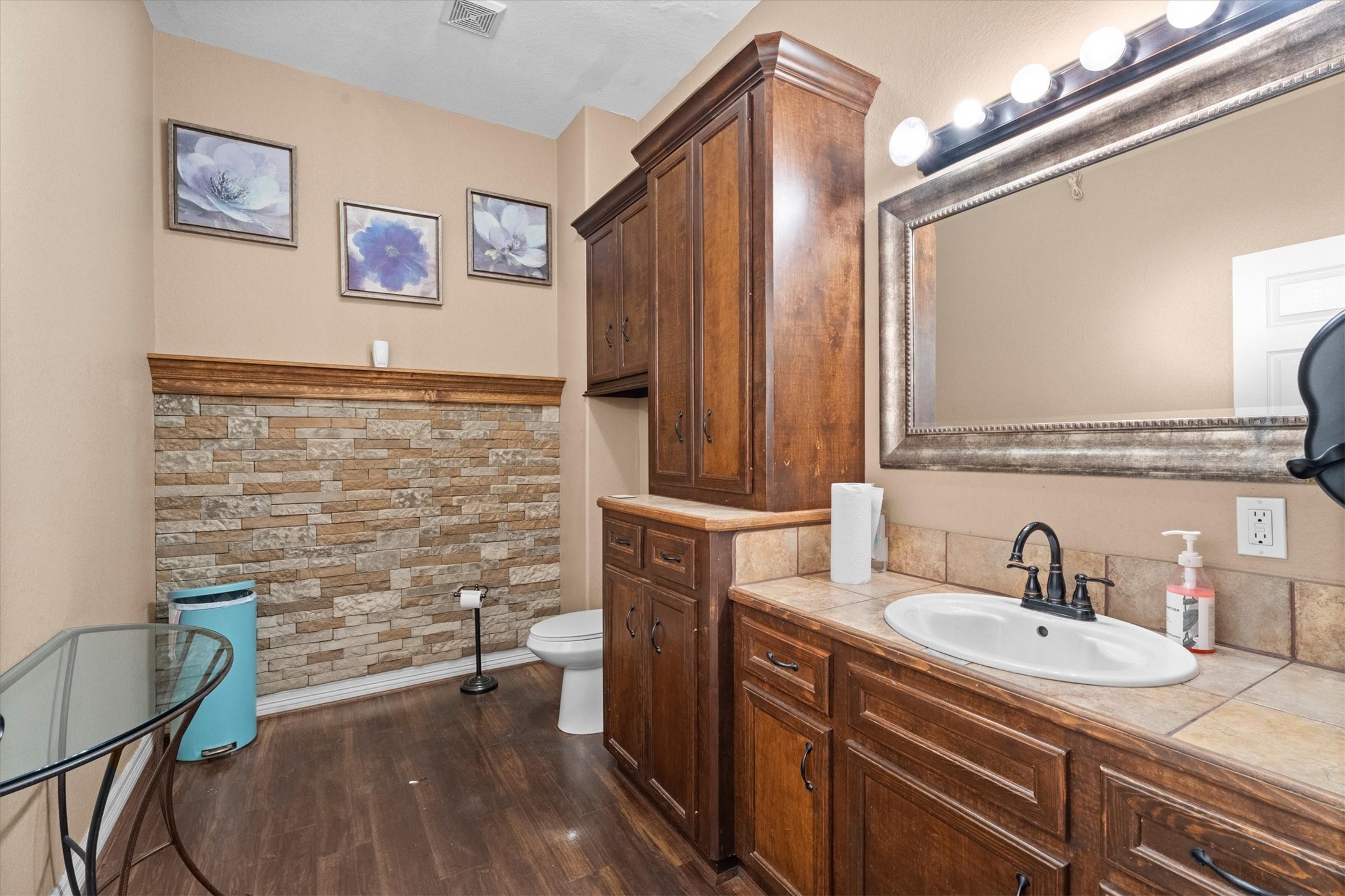 11066 Sh 242 Conroe, TX 77385 - Photo 12 of 21 This bathroom features elegant wooden cabinetry, a large framed mirror, and a single sink with a stylish faucet. The walls have a decorative stone accent, and the room is complemented by tasteful floral artwork.