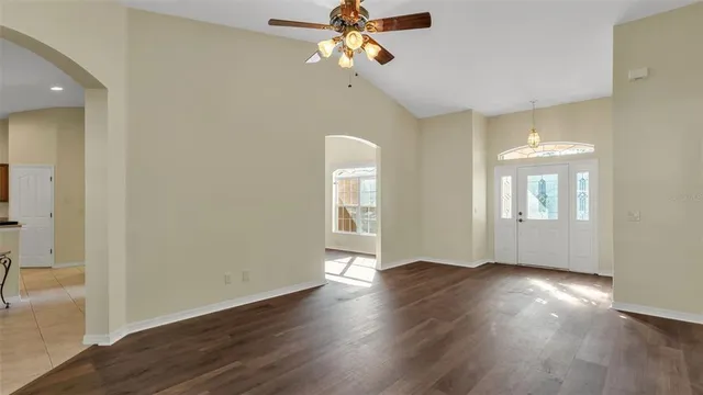 an empty room with wooden floor chandelier fan and windows