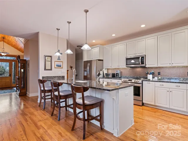 a kitchen with stainless steel appliances granite countertop a stove top oven a sink dishwasher and a refrigerator with wooden floor