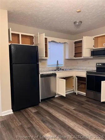 a kitchen with stainless steel appliances granite countertop a refrigerator a sink dishwasher a stove top oven a dining table and chairs with wooden floor