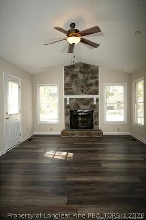 a living room with wooden floor a fireplace a ceiling fan and a rug