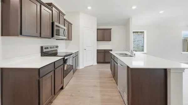 a kitchen with stainless steel appliances a stove top oven a sink a refrigerator white cabinets and wooden floor