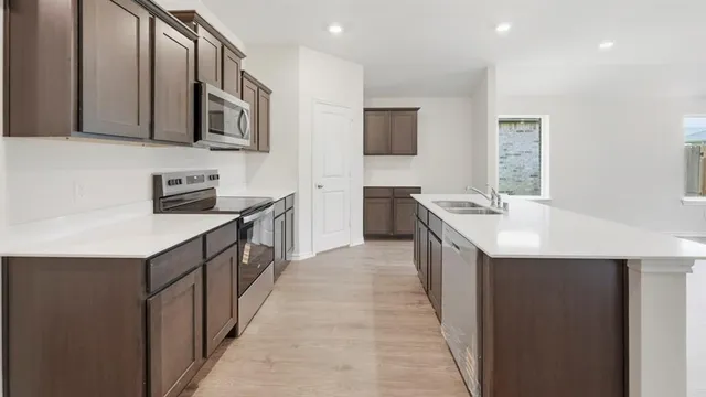 a kitchen with stainless steel appliances a stove top oven a sink a refrigerator white cabinets and wooden floor