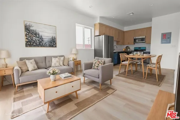 a living room with stainless steel appliances furniture a rug kitchen view and a window