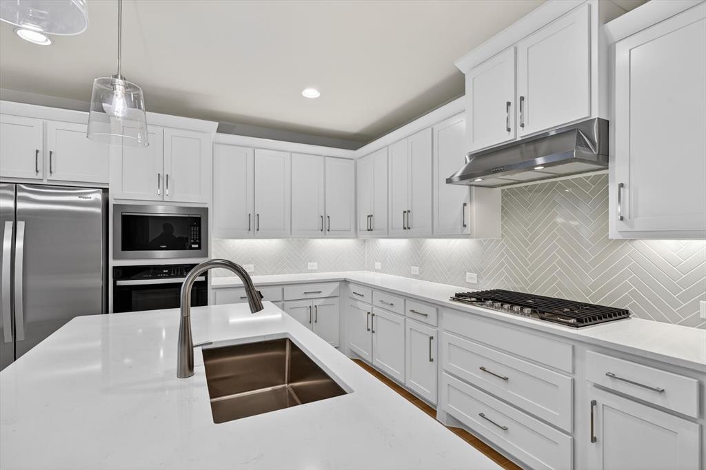 4123 Windy Point Court Oak Point, TX 75068 - Photo 16 of 29 Modern kitchen featuring white shaker cabinetry, stainless steel appliances, a herringbone tile backsplash, and light-toned countertops