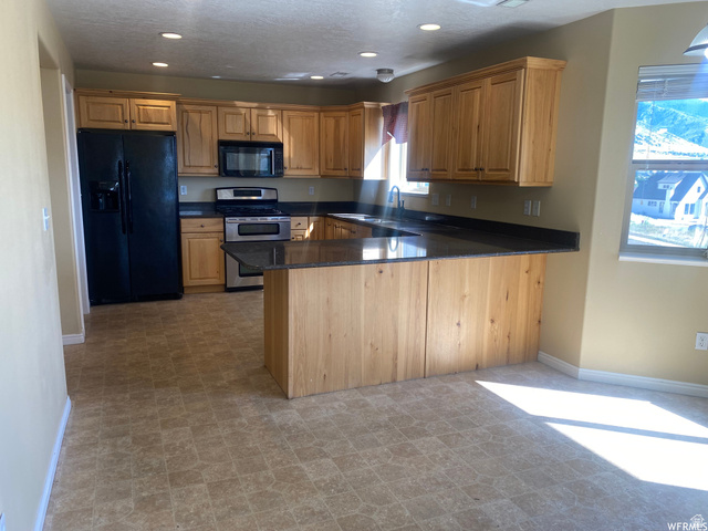 83 Canterbury Circle Logan, UT 84321 - Photo 3 of 23 Kitchen featuring black appliances, a peninsula, dark stone counters, recessed lighting, and wood finish cabinetry