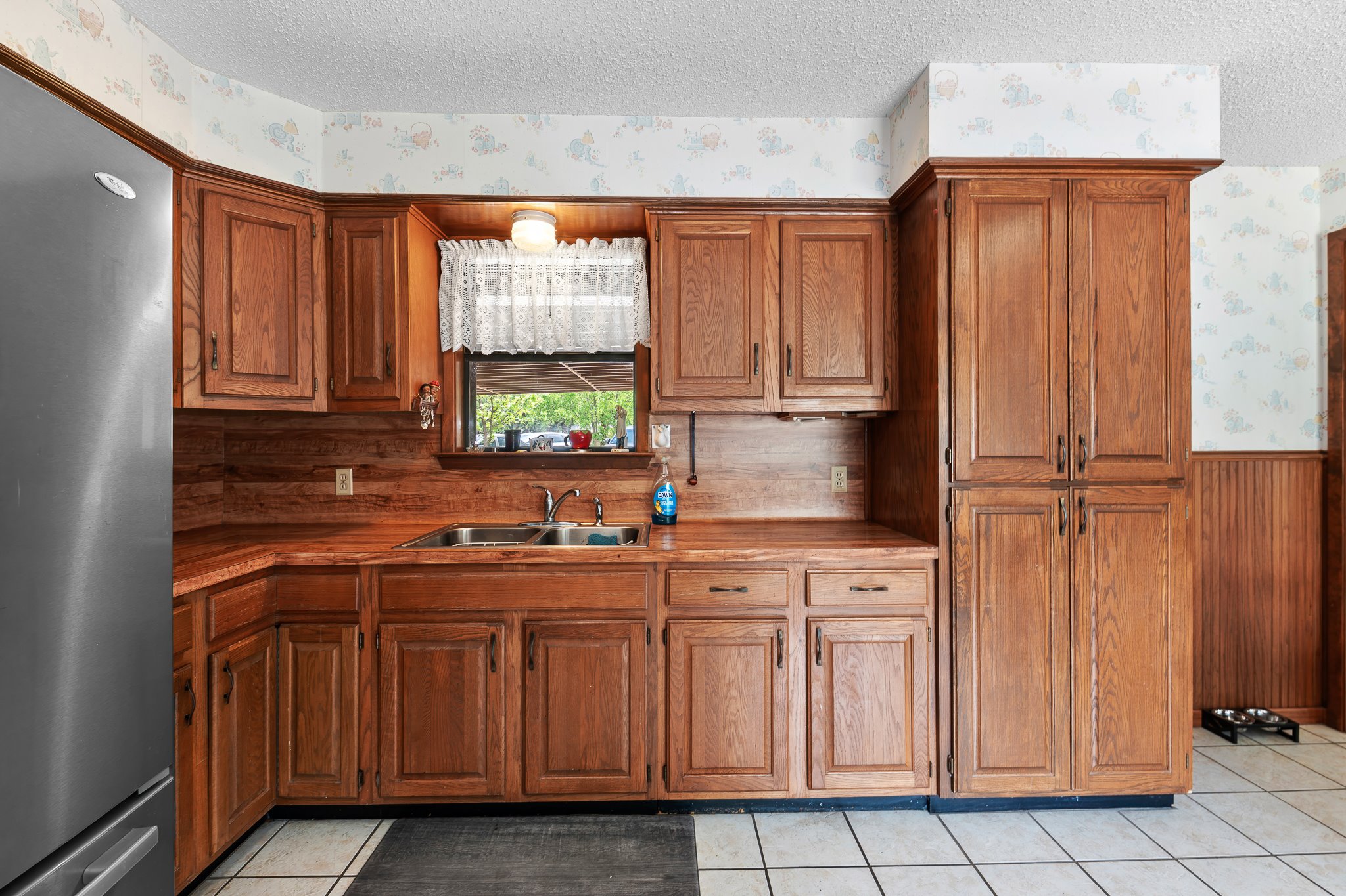 5600 Libyan Circle Austin, TX 78745 - Photo 14 of 37 Kitchen with wallpapered walls, freestanding refrigerator, wood finish cabinets, a wainscoted wall, and a textured ceiling