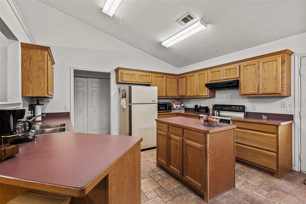 80 Campbell Road Sadler, TX 76264 - Photo 19 of 29 Kitchen with vaulted ceiling, electric appliances, under cabinet range hood, a center island, and light stone finish flooring