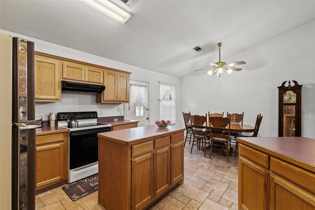 80 Campbell Road Sadler, TX 76264 - Photo 3 of 29 Kitchen with electric range oven, freestanding refrigerator, under cabinet range hood, stone finish flooring, island, bar seating and vaulted ceiling