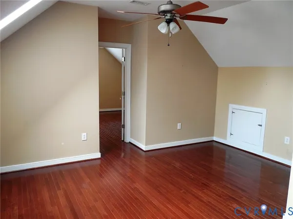 a view of an empty room with wooden floor and a ceiling fan