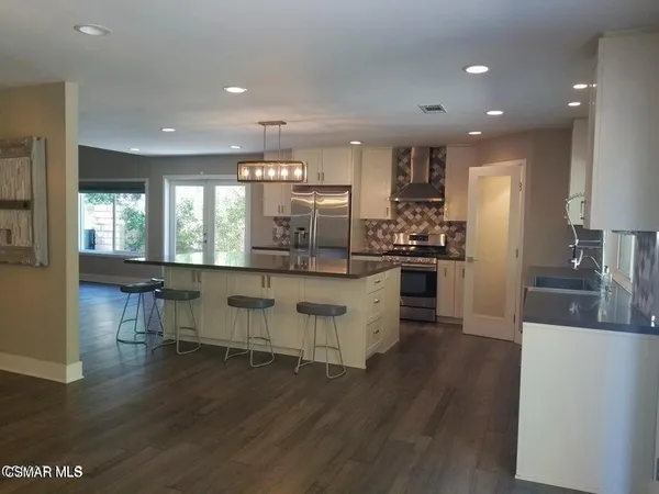 a kitchen with stainless steel appliances kitchen island granite countertop a stove a refrigerator a sink a dining table and chairs with wooden floor
