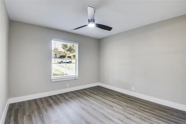 an empty room with wooden floor chandelier fan and windows