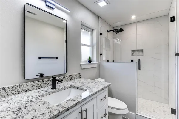 a bathroom with a granite countertop sink toilet mirror and shower
