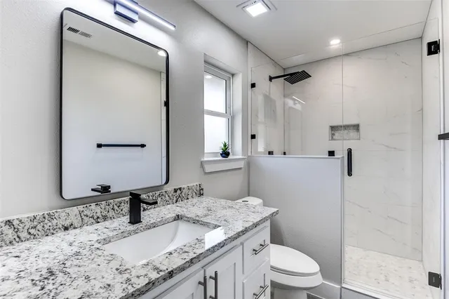 a bathroom with a granite countertop sink toilet mirror and shower
