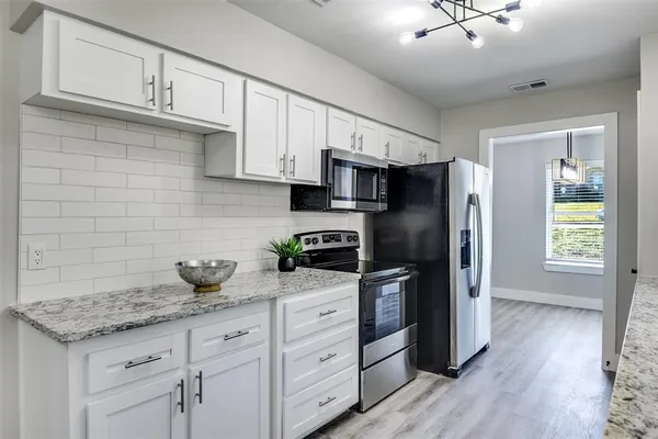 a kitchen with stainless steel appliances granite countertop a refrigerator a stove a sink dishwasher and white cabinets with wooden floor