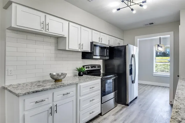 a kitchen with stainless steel appliances granite countertop a refrigerator a stove a sink dishwasher and white cabinets with wooden floor