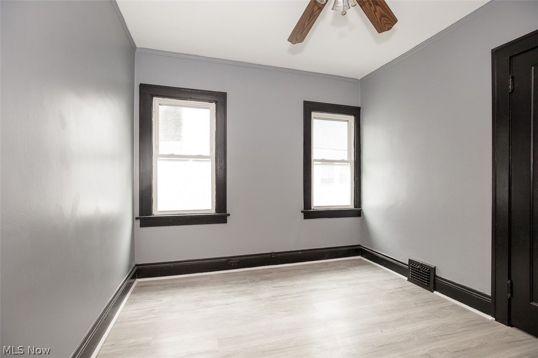 1868-1870 Lampson Road Cleveland, OH 44112 - Photo 13 of 36 Room featuring light gray walls with dark trim, dual windows, wood-finish flooring, and a ceiling fan