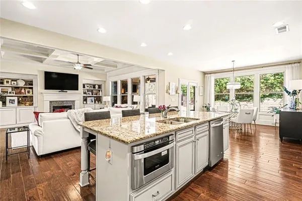 a open kitchen with stainless steel appliances granite countertop a stove top oven a sink dishwasher a dining table and chairs with wooden floor