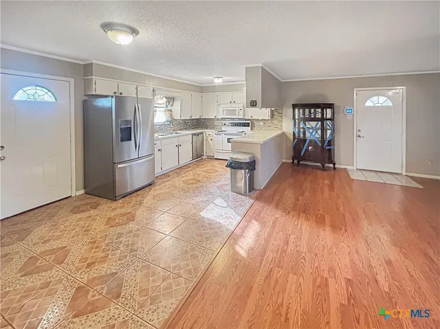 a large white kitchen with stainless steel appliances granite countertop a refrigerator oven a sink dishwasher and white cabinets with wooden floor
