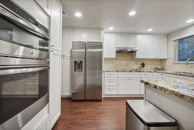 a kitchen with granite countertop cabinets stainless steel appliances a sink and wooden floor