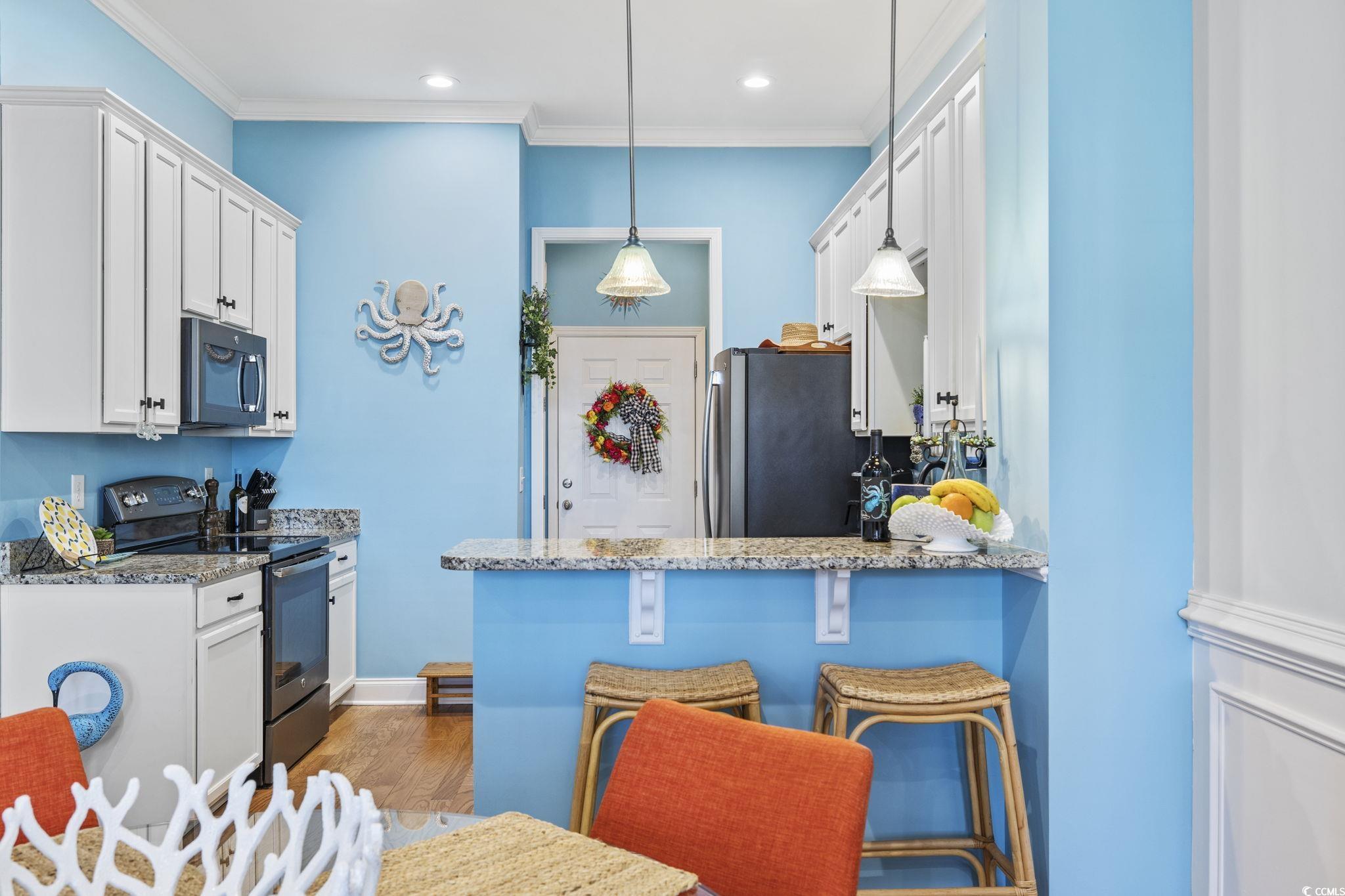 718 Shine Avenue, Unit 718 Myrtle Beach, SC 29577 - Photo 12 of 36 Kitchen with appliances with stainless steel finishes, a breakfast bar area, white cabinets, light stone countertops, and ornamental molding