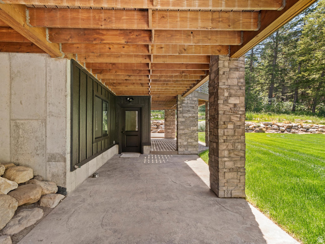 1225 Old Oregon Road Soda Springs, ID 83276 - Photo 47 of 67 Covered patio with stamped concrete flooring, wood beam ceiling, stone-clad pillars, a dark wood-paneled exterior wall, and a full-light entry door