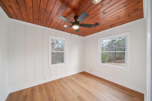 an empty room with wooden floor chandelier fan and windows