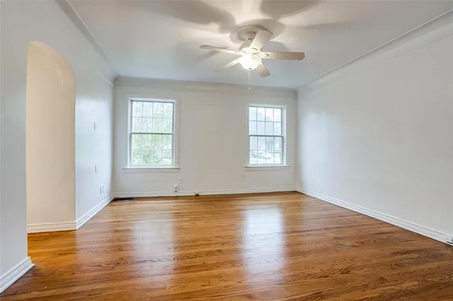 an empty room with wooden floor chandelier fan and windows