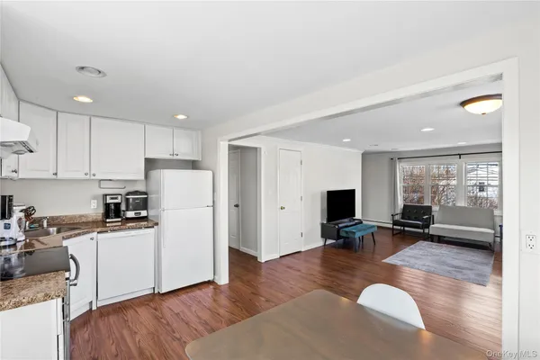 a kitchen with a refrigerator a stove top oven a sink dishwasher and couches with wooden floor