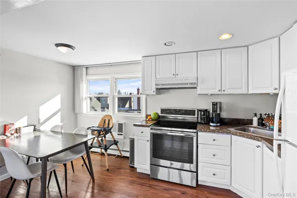 a kitchen with granite countertop a stove a sink a refrigerator and white cabinets with wooden floor