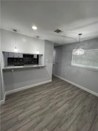 an empty room with wooden floor and kitchen view